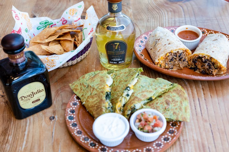 A delicious Mexican feast with burritos, quesadillas, salsa, and tequila, perfect for a rustic dining experience.