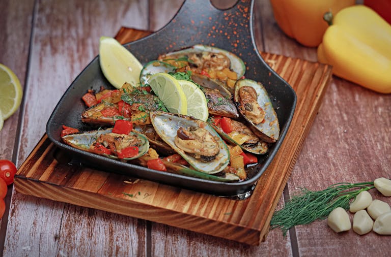 A savory mussel dish garnished with fresh lemon, dill, and peppers, perfect for seafood lovers.