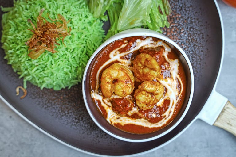 Close-up of spicy prawn curry with vibrant green herbed rice, garnished beautifully.