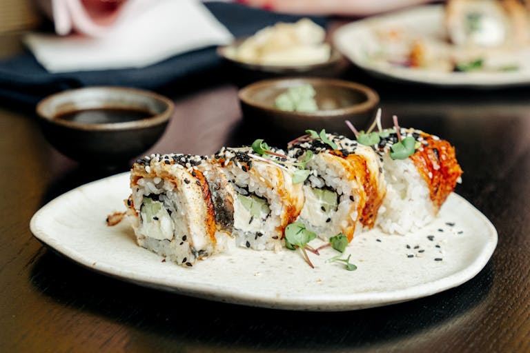 Close-up of sushi rolls with garnish and sauce display on a plate.