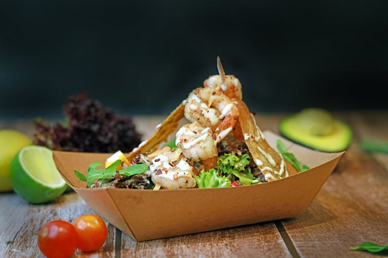 Delicious shrimp taco salad in a paper box with fresh veggies and avocado.