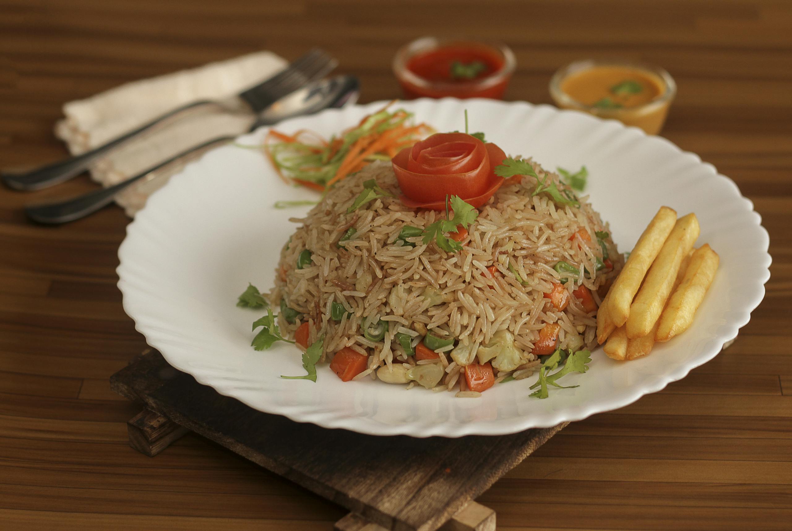 Tasty vegetable fried rice with a tomato rose and fries on a wooden background.